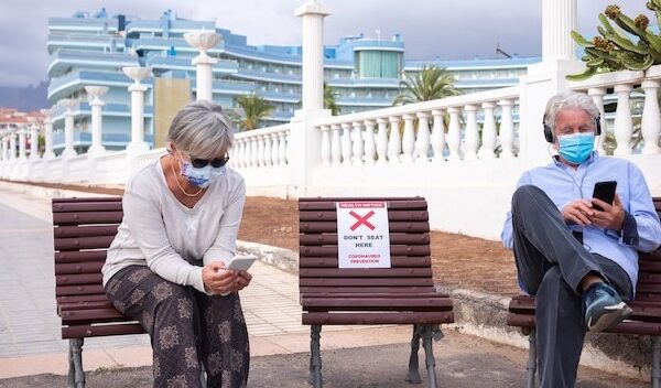 Social distancing concept. Two senior people sitting outdoor on allowed bench, using mobile phone