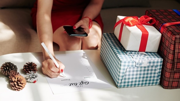 Close-up image of young woman checking smatphone when making gift list