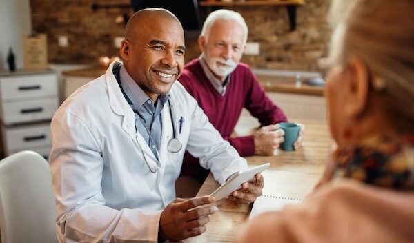 Happy black doctor using touchpad during a visit at mature couple's home