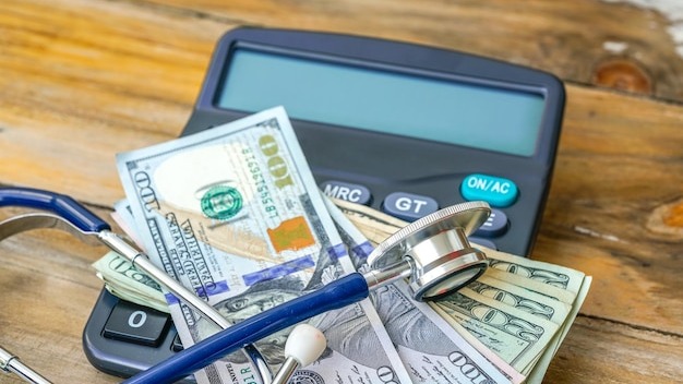 Close-up of calculator with stethoscope and paper currencies on table