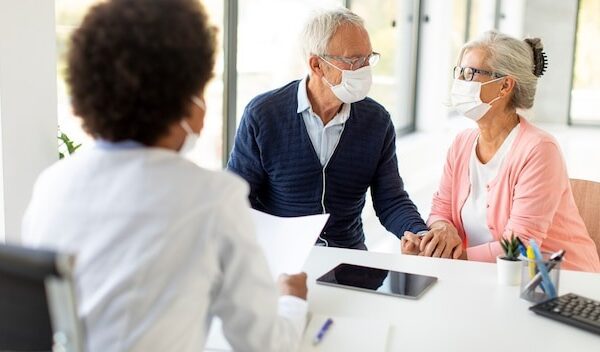 Senior couple with protective facial masks receive news from black female doctor in the office