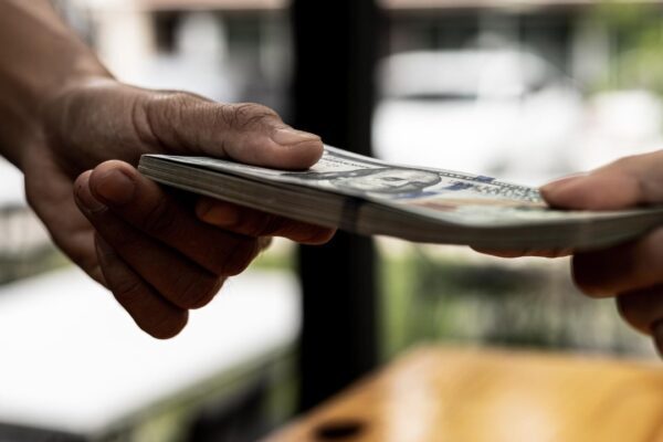 Two people are handing each other dollar bills, they are mutually beneficial business partners, they commit bribery fraud for business interests. The concept of corruption and bribery.