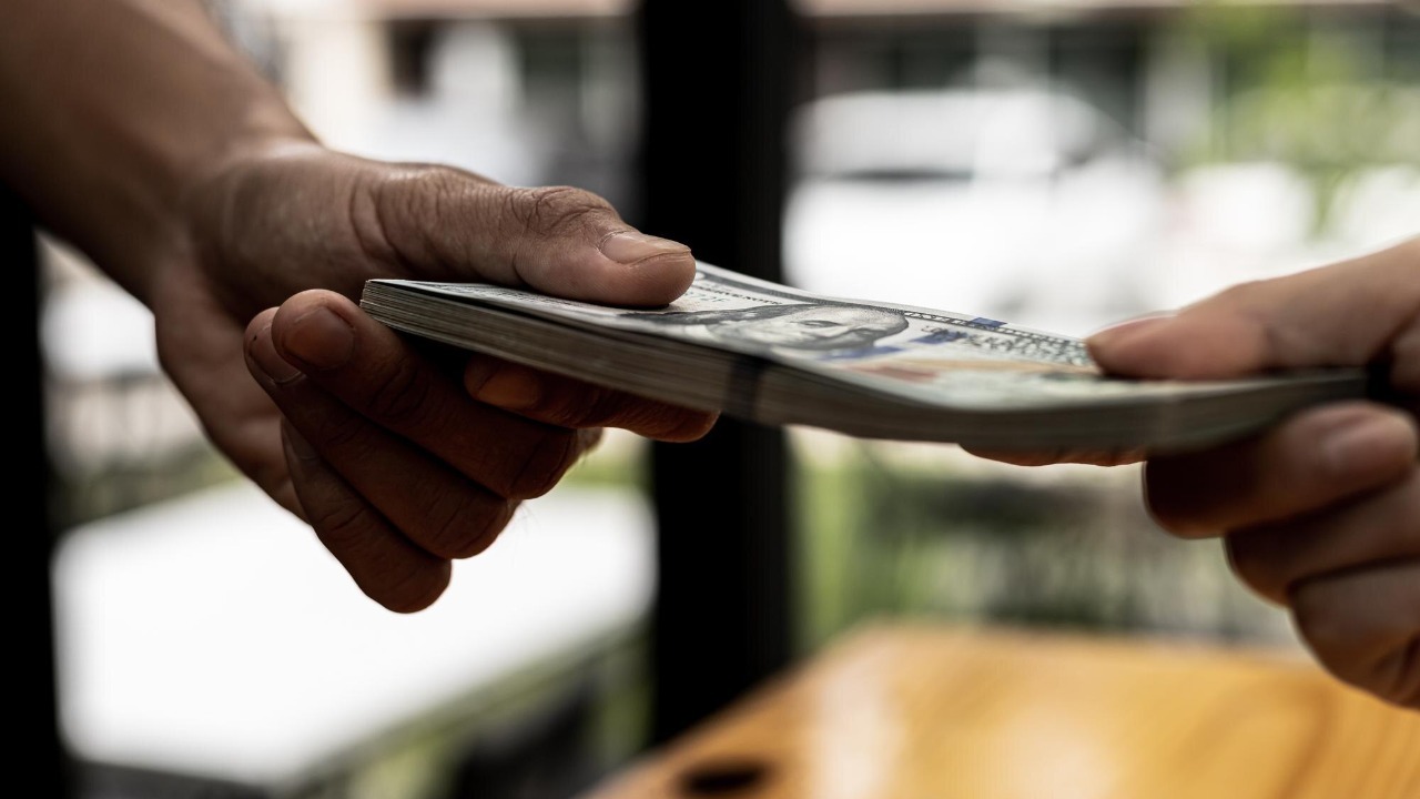 Two people are handing each other dollar bills, they are mutually beneficial business partners, they commit bribery fraud for business interests. The concept of corruption and bribery.