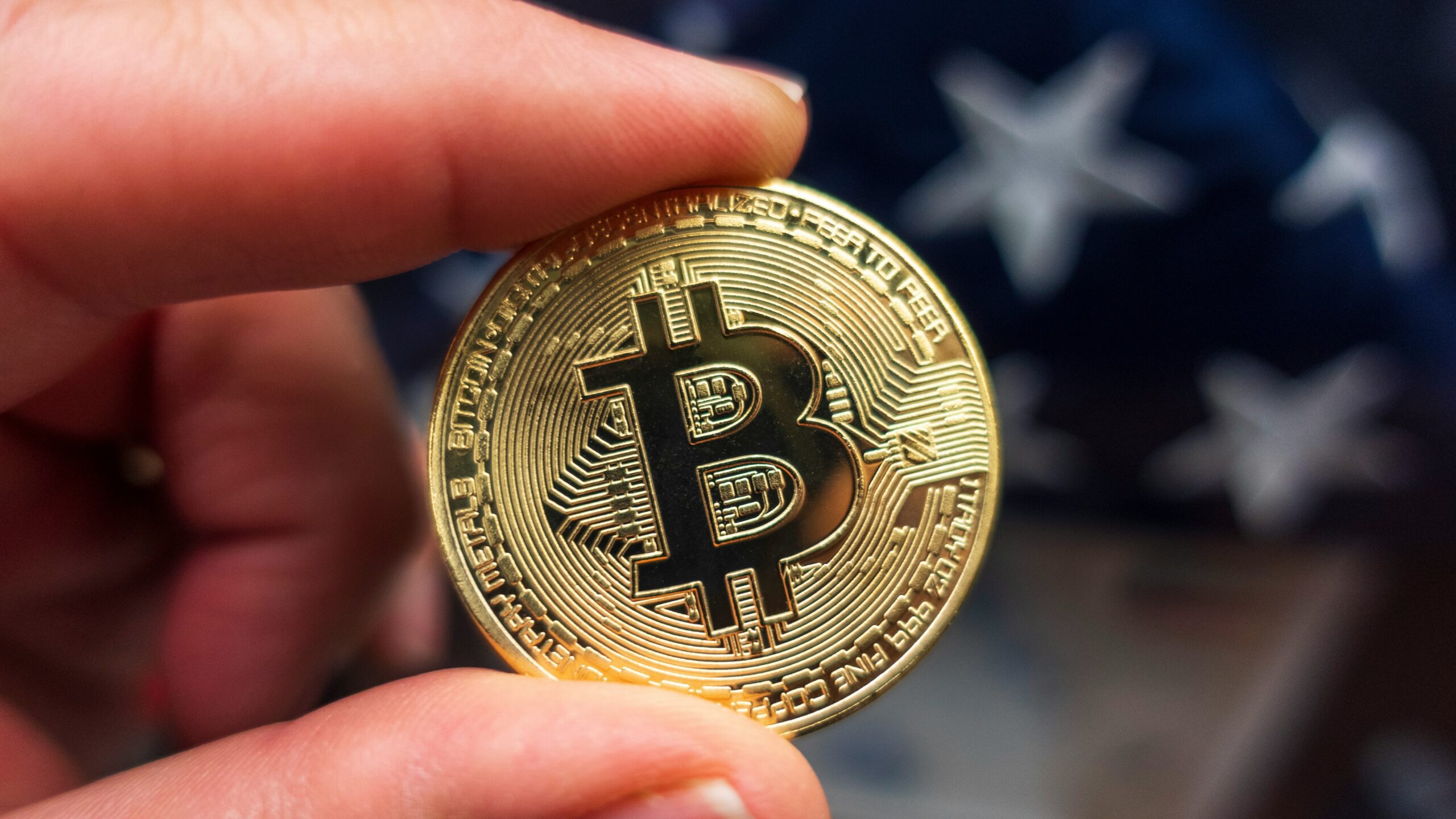 a hand holding a bit coin in front of an american flag