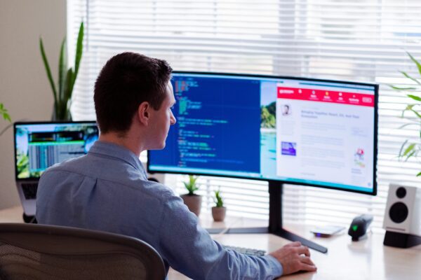 man in gray dress shirt sitting on chair in front of computer monitor