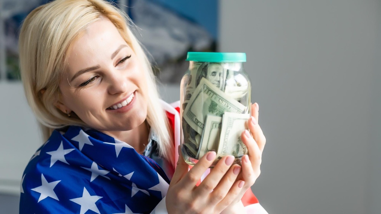 woman holding dollars in glass jar and american flag.