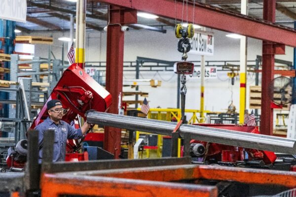 Worker operating heavy machinery in a factory, moving steel bars. Industrial scene indoors.