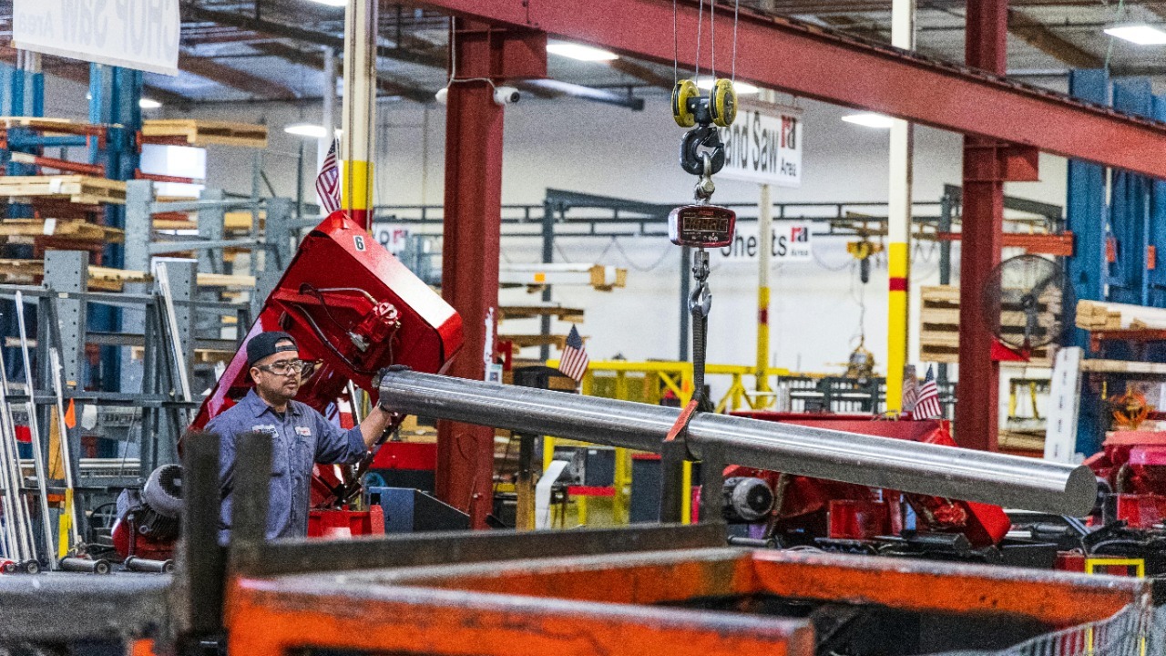 Worker operating heavy machinery in a factory, moving steel bars. Industrial scene indoors.