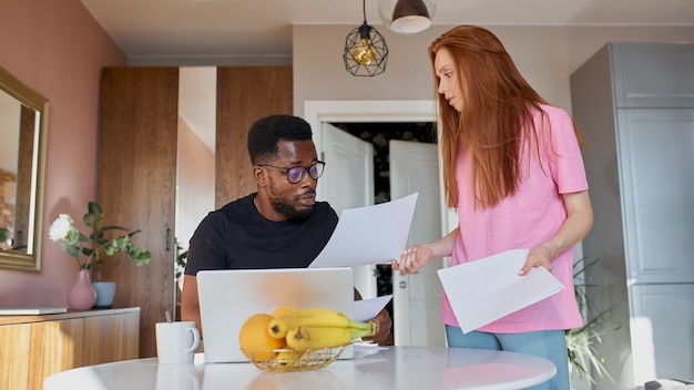 Serious african man read papers and caucasian woman discuss unpaid internal bills