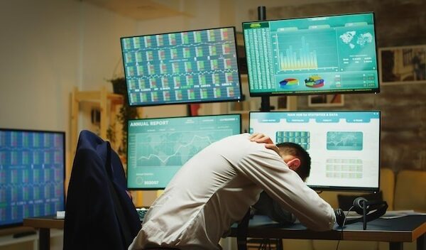 Angry stock market trader throwing graphs because of money loss in his home office with multiple displays presenting real time data of stock market