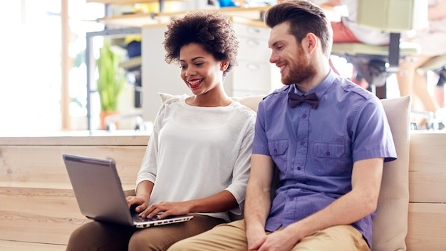 business, startup and people concept - happy creative team with laptop computer and folder in office