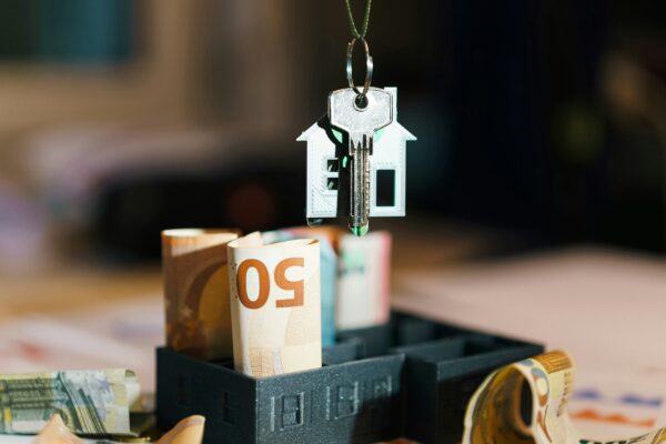 A house hanging from a string on top of a pile of money