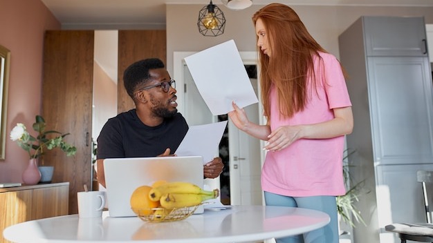 Interracial couple reading mail and checking accounting in the kitchen at home