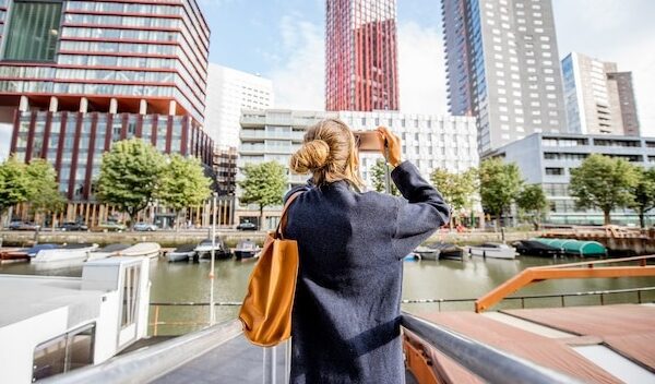 Young woman photographing modern skyscrapers standing on the harbor in Rotterdam city