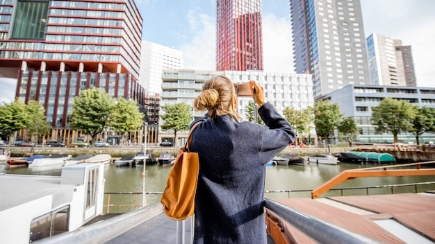 Young woman photographing modern skyscrapers standing on the harbor in Rotterdam city