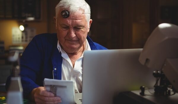 Horologist looking at notepad with laptop on table
