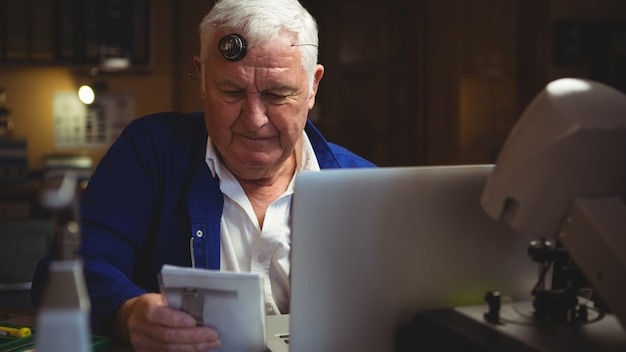Horologist looking at notepad with laptop on table