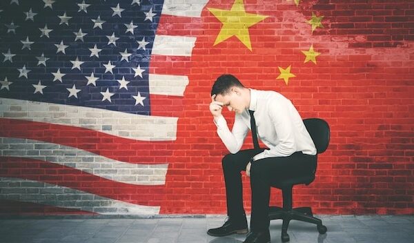 Stressed businessman sits with China and USA flag