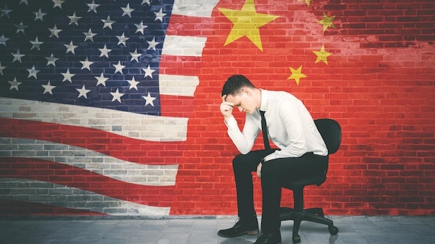 Stressed businessman sits with China and USA flag