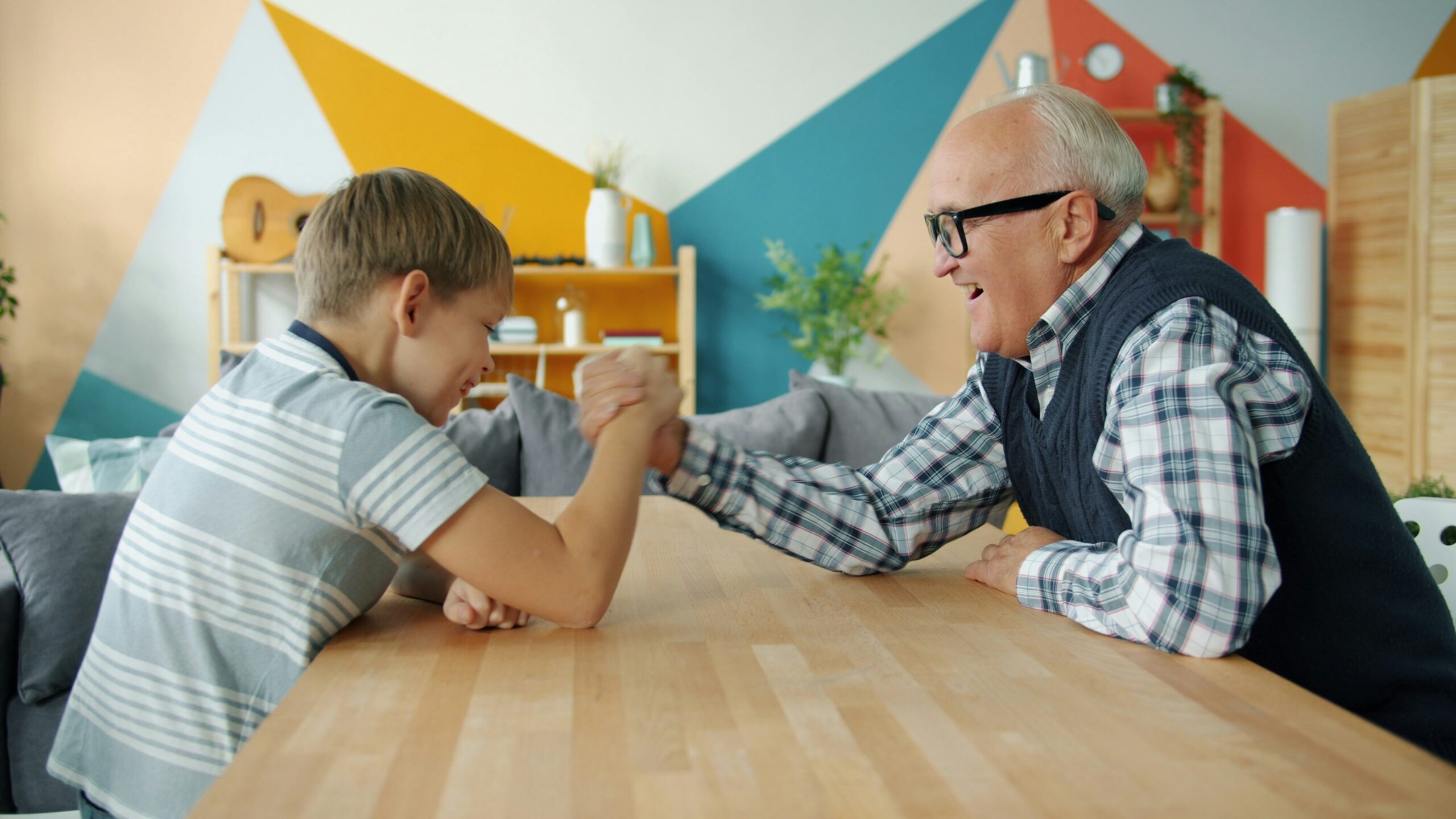 Grandfather and grandson arm wrestling at table