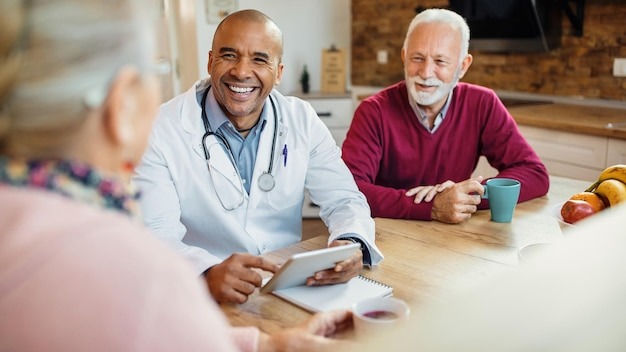Happy African American doctor talking to senior couple during home visit