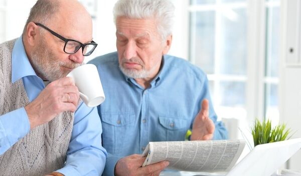 Two senior men sitting at table and reading newspaper