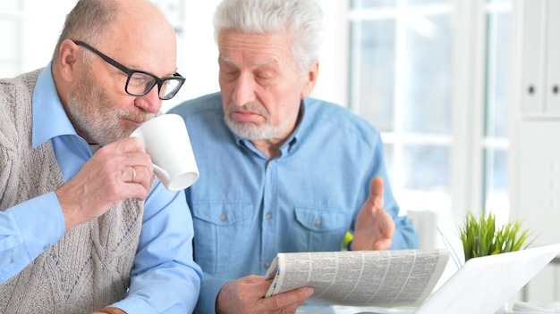 Two senior men sitting at table and reading newspaper