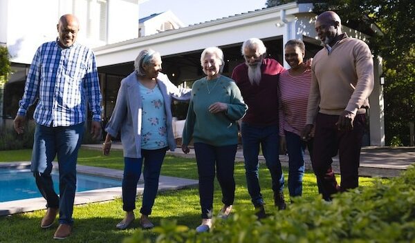 Happy diverse group of senior friends walking next to pool in sunny garden