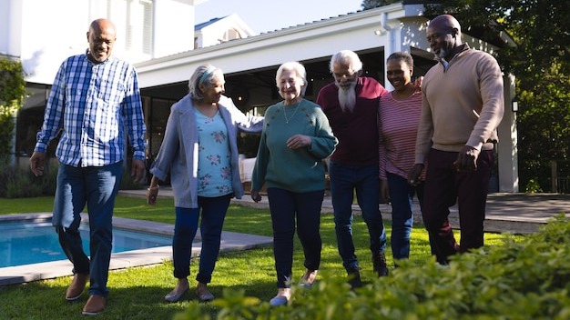 Happy diverse group of senior friends walking next to pool in sunny garden