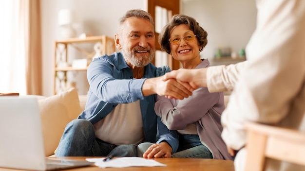 Satisfied senior spouses making sale purchase deal handshaking with real estate agent agreeing to