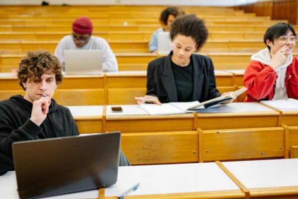 A diverse group of college students studying in a classroom setting with laptops and books.