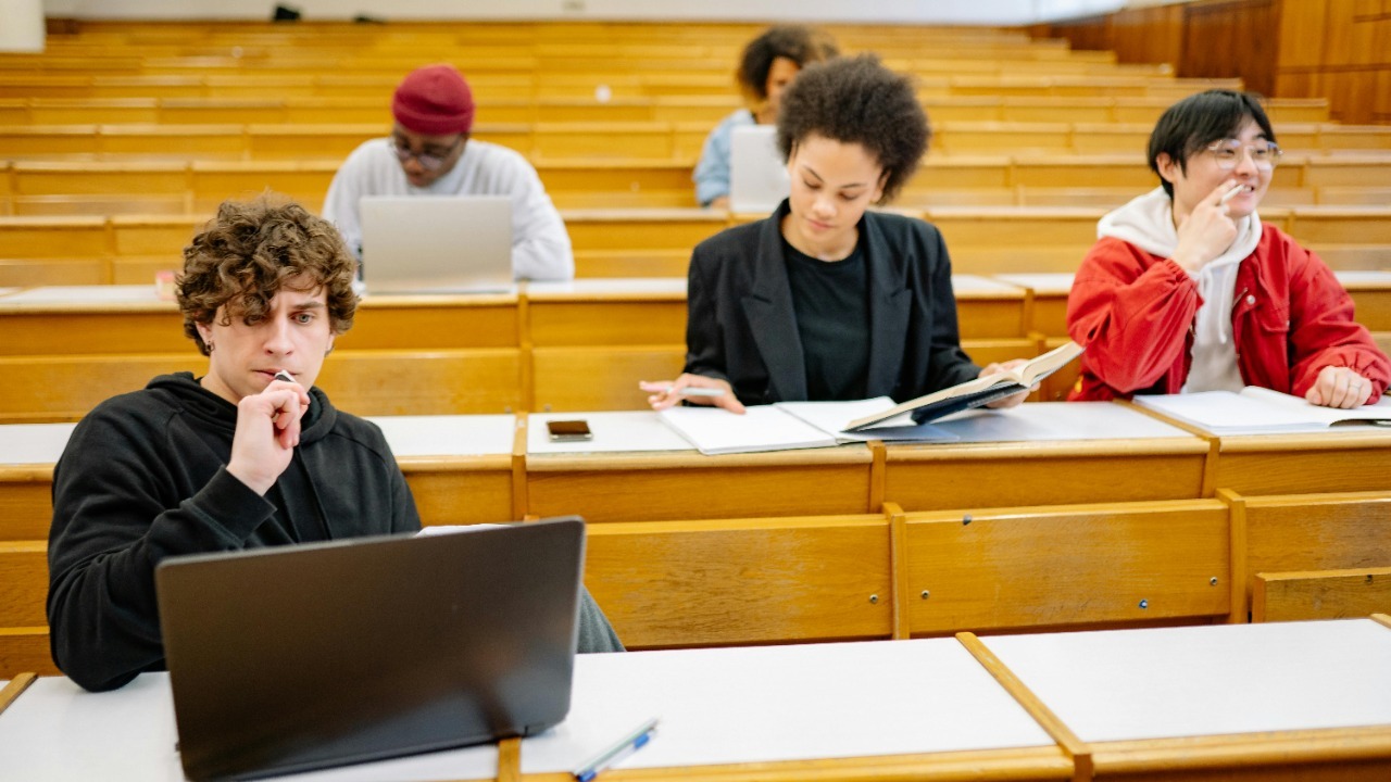 A diverse group of college students studying in a classroom setting with laptops and books.