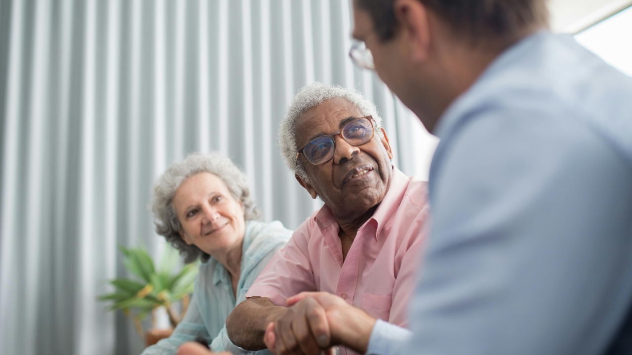 Elderly couple discussing with a consultant indoors, expressing interest and connection.