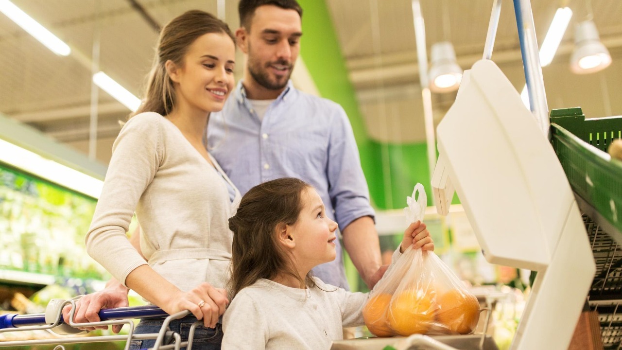 shopping, sale, consumerism and people concept – happy family with child weighing oranges on scale at grocery store