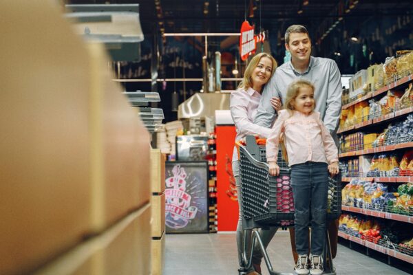 Family enjoying a shopping trip in a supermarket, with a child in a cart and parents smiling.