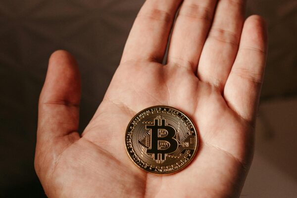 Close-up image of a person's hand holding a Bitcoin coin, symbolizing cryptocurrency and finance.