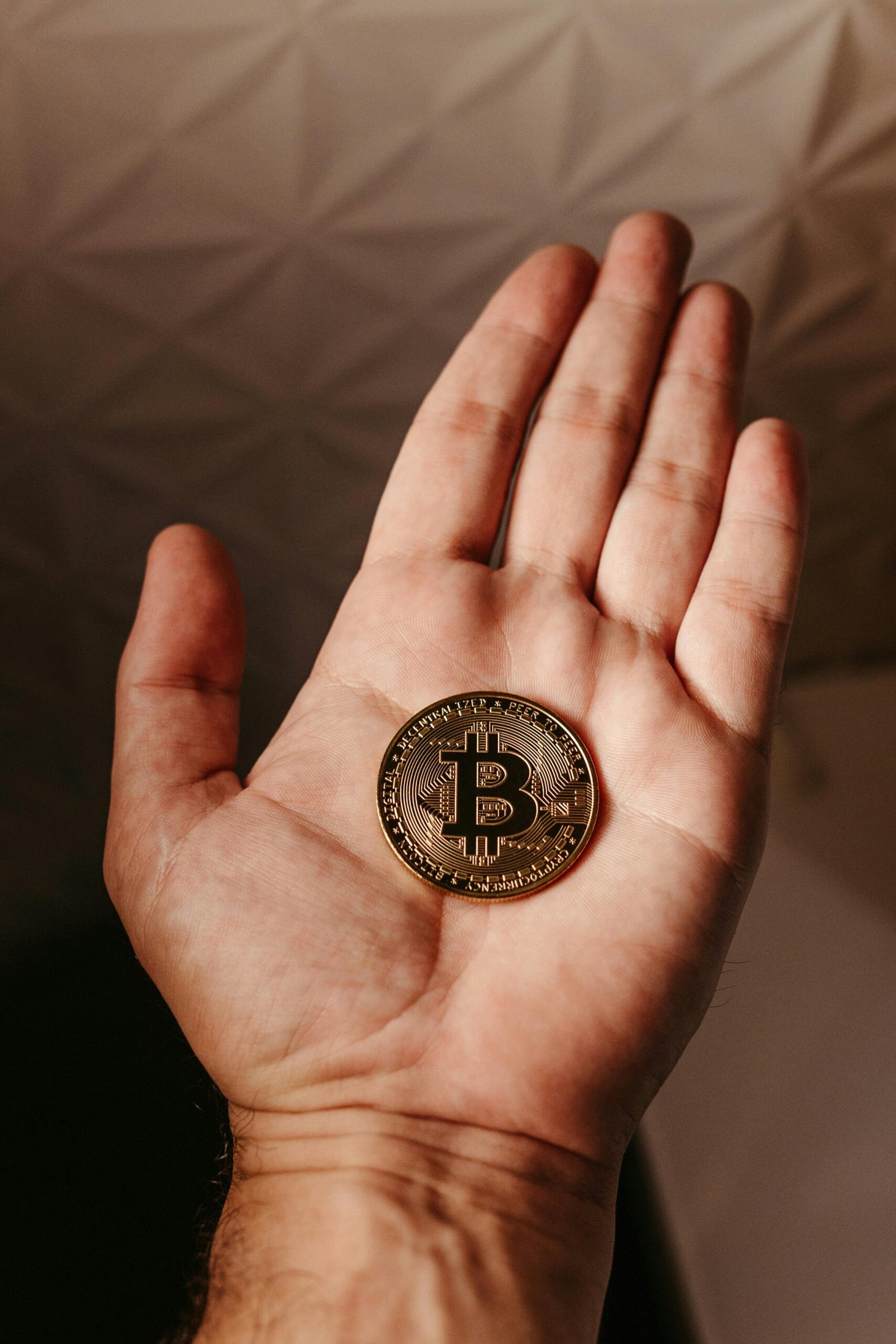 Close-up image of a person's hand holding a Bitcoin coin, symbolizing cryptocurrency and finance.