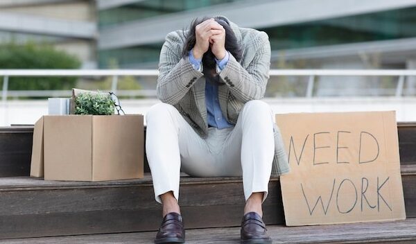 Unhappy japanese businessman sits outside next to sign need work