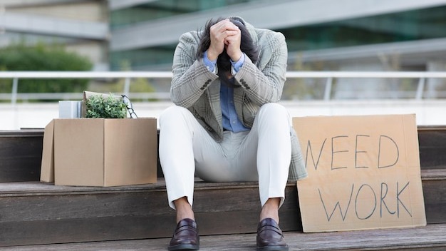 Unhappy japanese businessman sits outside next to sign need work
