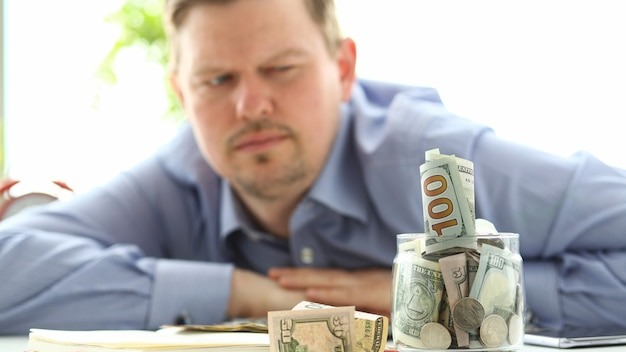 Man looking at jar full of money thinking about his debts