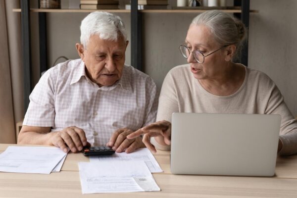 Concentrated middle aged mature family couple calculating domestic expenditures or taxes managing monthly budget paying taxes or bills in computer ebanking application planning investment