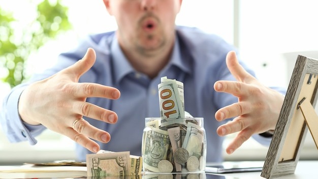 Male hands grabbing big fat jar full of US currency as greed gesture