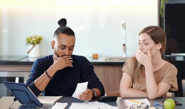 Young mixed-race couple covering mouth as they are shocked with sum in unpaid bill