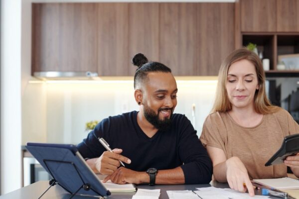 Young couple sitting at kitchen table and checking bills and paychecks and calculating family expences
