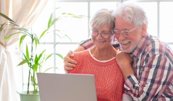 Beautiful caucasian senior couple with eyeglasses browsing together on laptop sitting at home old retirees people enjoying tech and social