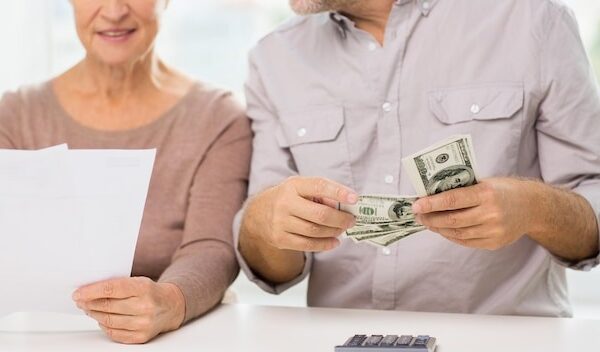 family, business, savings age and people concept - close up of smiling senior couple with bills, dollar money and calculator at home