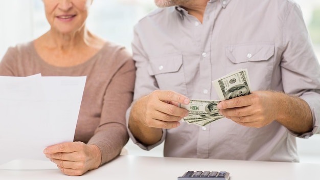family, business, savings age and people concept - close up of smiling senior couple with bills, dollar money and calculator at home