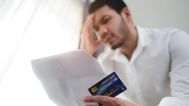 stressed Asian man holding credit card and bill