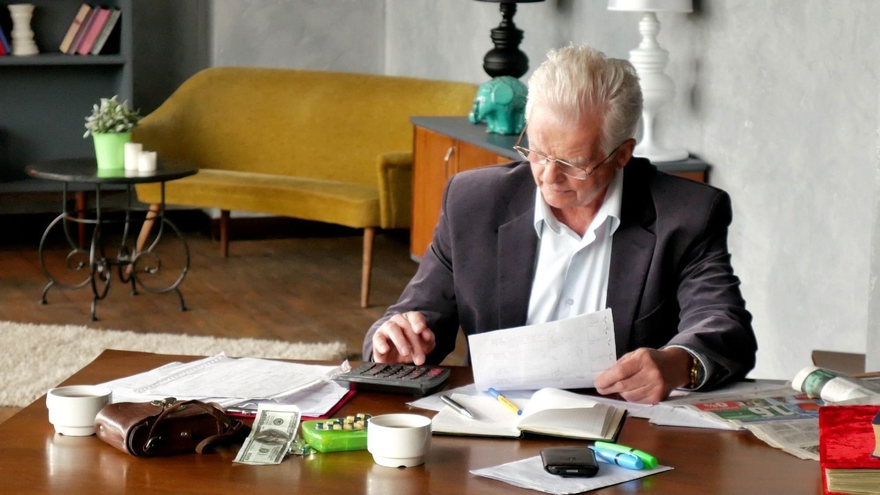 Senior man with papers or bills and calculator at home in evening
