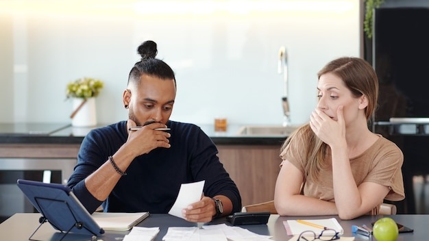 Young mixed-race couple covering mouth as they are shocked with sum in unpaid bill